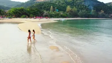 Deniz suyunda yürüyen bikinili iki genç kız arkadaş. Tropik tatil köyünde dinlenen güzel kadınlar