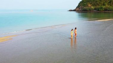 Deniz suyunda yürüyen bikinili iki genç kız arkadaş. Tropik tatil köyünde dinlenen güzel kadınlar