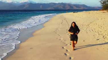 Sırt çantalı bir kadın sahilde yürüyor.