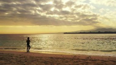 Endonezyalı balıkçı elinde uzun bir değnekle, alevli günbatımında denizde duruyor, Sanur, Bali