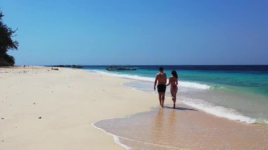 Genç ve güzel bir çiftin güzel bir okyanus videosunun yanında tatilin tadını çıkardığı tropik ada sahnesi. 