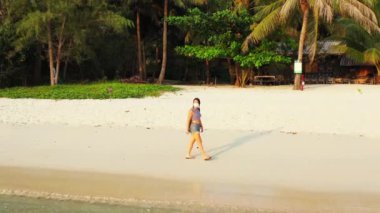 Kumsalda yürüyen maskeli bir kızın görüntüsü. 