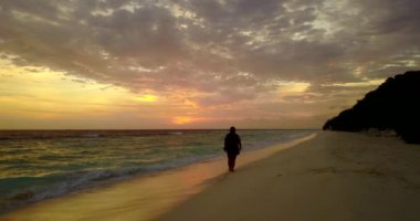 Gün batımında kumsalda yürüyen bir kadın silueti.