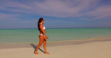 Beyaz bikinili güzel bir kadın güzel bir tropikal sahilde yürüyor masmavi su ve beyaz kumla.