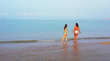 Deniz suyunda yürüyen bikinili iki genç kız arkadaş. Tropik tatil köyünde dinlenen güzel kadınlar