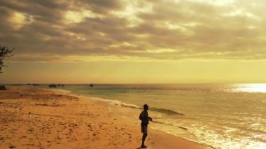 Endonezyalı balıkçı elinde uzun bir değnekle, alevli günbatımında denizde duruyor, Sanur, Bali