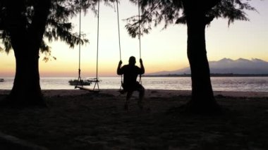 Sahilde sallanan bir kadın silueti.