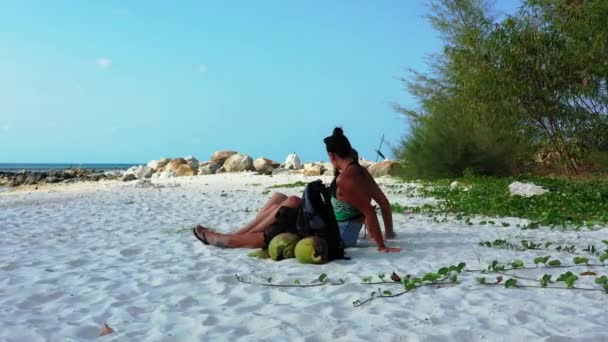 Két fiatal barátnő ül a homokos tengerparton, zacskókkal a mellettük és beszélgetnek. Gyönyörű nők pihennek trópusi üdülőhelyen   