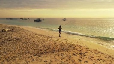Endonezyalı balıkçı elinde uzun bir değnekle, alevli günbatımında denizde duruyor, Sanur, Bali