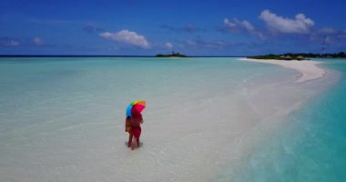 Genç bir adam ve kadın güneş şemsiyesiyle deniz suyunda yürüyorlar. Tropik bir tatil köyünde dinlenen güzel bir çift.   