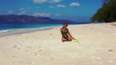 Tropik plajda akıllı telefon kullanan güzel genç bir kadın.