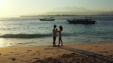 Genç çift, kristal okyanus suyunun yanındaki kumlu tropik plajda dinleniyor. Güzel sahil şeridi, güzel bir çift dinleniyor. 