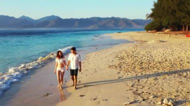 Genç çift, kristal okyanus suyunun yanındaki kumlu tropik plajda dinleniyor. Güzel sahil şeridi, güzel bir çift dinleniyor. 