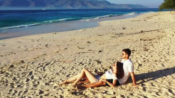美しい海の近くの熱帯の砂浜に若い素敵なカップルに座っています 夏の旅行のコンセプト — ストック動画