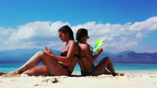 2人の女の子が楽しい時間を過ごし砂浜でパンフレットを読み — ストック動画