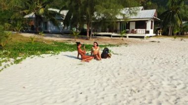 Bikinili iki genç kız arkadaş kumlu deniz kıyısında yatıyorlardı. Bir kız, kız arkadaşının fotoğrafını cep telefonuyla çekiyor. Tropik tatil köyünde dinlenen güzel kadınlar 