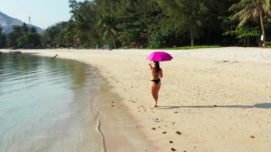 Siyah bikinili genç çekici kız kumlu sahilde yürüyor, yaz tatili konsepti  