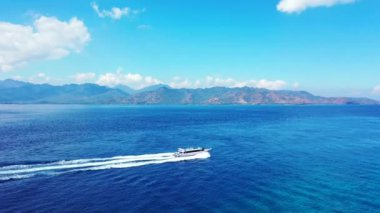 Dağların arkasında mavi denizde hareket eden küçük bir yat. Endonezya, Bali 'ye seyahat.
