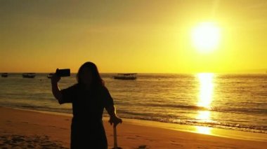 Tayland 'da gün batımında güzel plajda fotoğraf çeken bir kadın..