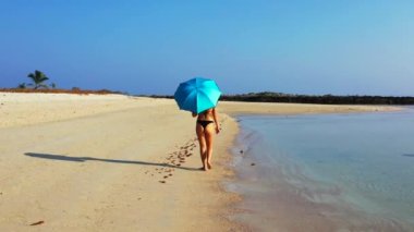 Kumsalda şemsiyeyle yürüyen bikinili seksi kız. Yaz tatili konsepti.  