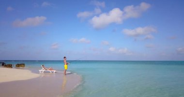 Erkek balık tutarken kız arkadaşı adanın sahilinde dinleniyor. 