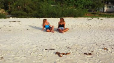 Tropikal adanın kumlu kumsalında oturan güzel beyaz kızlar 