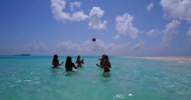 Sahilin yakınındaki turkuazlı berrak sularda top oynayan kızların videosu.  