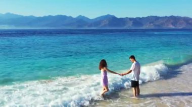 Çekici kız arkadaşıyla turkuaz kristal okyanus suyunun önünde dinlenen bir adam, yaz tatili konsepti. 