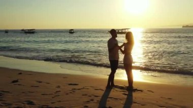 Okyanus ve tropikal sahilde dramatik bir gün batımı. Kıyı şeridinde duran genç çift, seyahat kavramı 