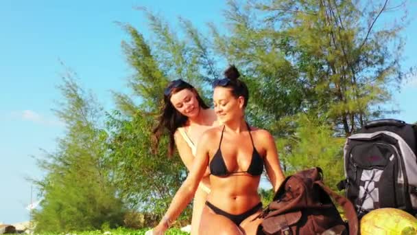 两个年轻的女朋友坐在沙滩上 晒日光浴 一个女孩把防晒霜弄脏了她的女朋友 美丽的女人在热带度假胜地休息 — 图库视频影像