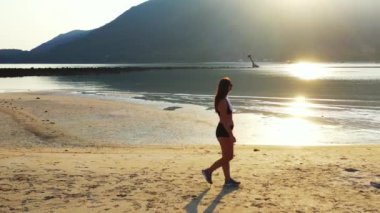Mayo giymiş çekici genç bir kadın. Güzel adanın okyanusu yakınında dinleniyor, yürüyor ve kulaklıkla müzik dinliyor. 