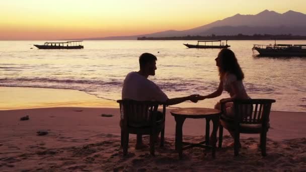 Романтическая Пара Сидящая Стульях Возле Стола Наслаждающаяся Закатом Тропическом Пляже — стоковое видео