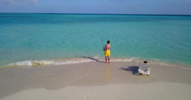 Erkek balık tutarken kız arkadaşı adanın sahilinde dinleniyor. 