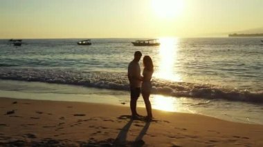 Okyanus ve tropikal sahilde dramatik bir gün batımı. Kıyı şeridinde duran genç çift, seyahat kavramı 