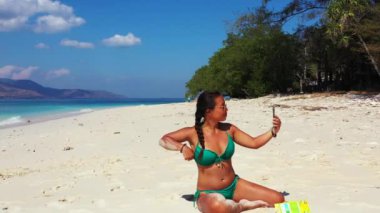 Tropik plajda akıllı telefon kullanan güzel genç bir kadın.