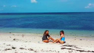 İki kızın kumsalda oturup birbirleriyle konuşarak güzel vakit geçirmesini izlemek.