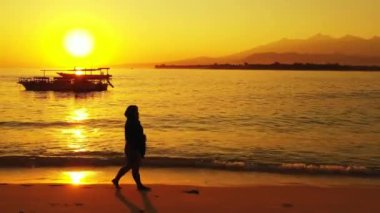  Gün batımında sahilde yürüyen bir kadın.