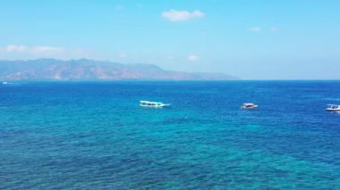 Arka planda sisli dağlar ve tekneler olan mavi deniz manzarası. Gili Trawangan, Endonezya 'nın doğal manzarası.