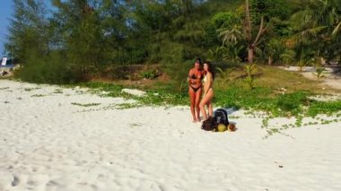 Bikinili iki genç kız, kumlu deniz kıyısında durup cep telefonuyla selfie çekiyorlar. Tropik tatil köyünde dinlenen güzel kadınlar 