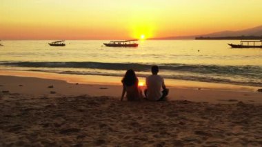 Akşamları kumsalda oturup sohbet eden bir çiftin görüntüsü.