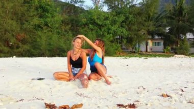 Tropikal adanın kumlu kumsalında oturan güzel beyaz kızlar 