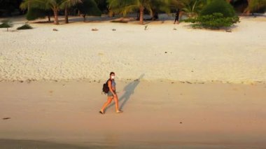 Kumsalda yürüyen maskeli bir kızın görüntüsü. 