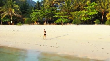 Mayo giymiş çekici genç bir kadın. Güzel adanın okyanusu yakınında dinleniyor, yürüyor ve kulaklıkla müzik dinliyor. 