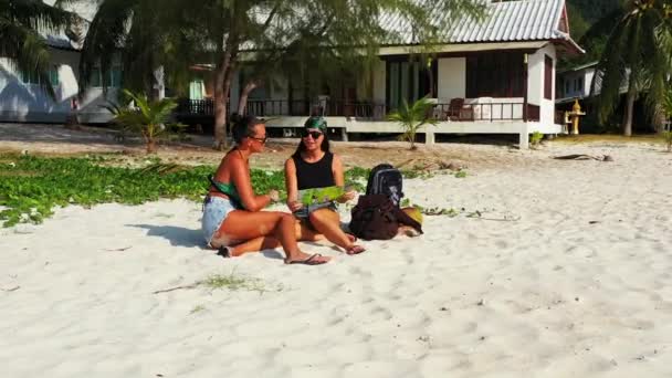 Две Юные Подруги Сидят Песчаном Побережье Багажом Рядом Наблюдая Картой — стоковое видео