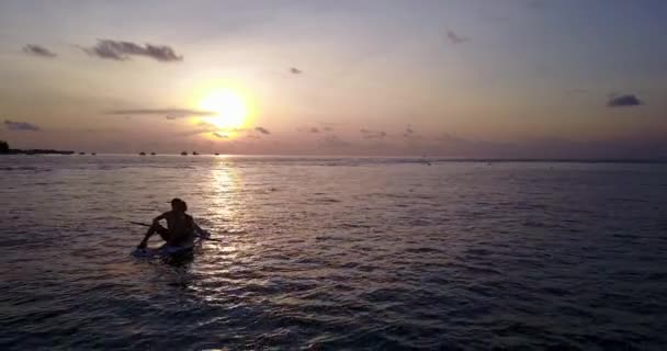 日没に海で一緒にサーフィンをしているカップルの映像です — ストック動画