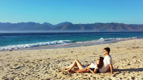 美しい海の近くの熱帯の砂浜に若い素敵なカップルに座っています 夏の旅行のコンセプト — ストック動画