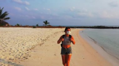 Kumsalda yürüyen maskeli bir kızın görüntüsü. 