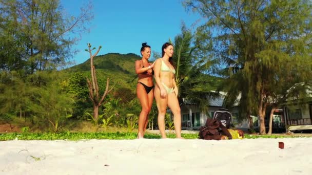 砂の海の海岸 日光浴や話に立って2人の若い女の子の友人 ある女の子が女の子の友人に太陽のクリームを塗りました 熱帯リゾートにいる美しい女性 — ストック動画