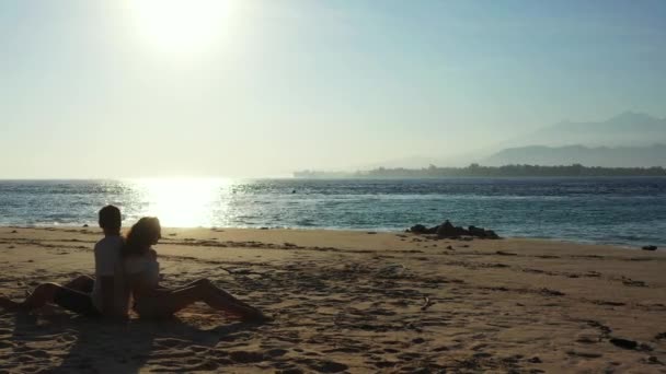 美しい海の近くの熱帯の砂浜に若い素敵なカップルに座っています 夏の旅行のコンセプト — ストック動画