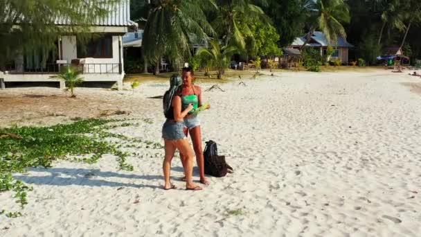两个年轻的女朋友站在沙滩上 身边背着行李 看着地图 为将来的旅行和谈话做准备 美丽的女人在热带度假胜地休息 — 图库视频影像
